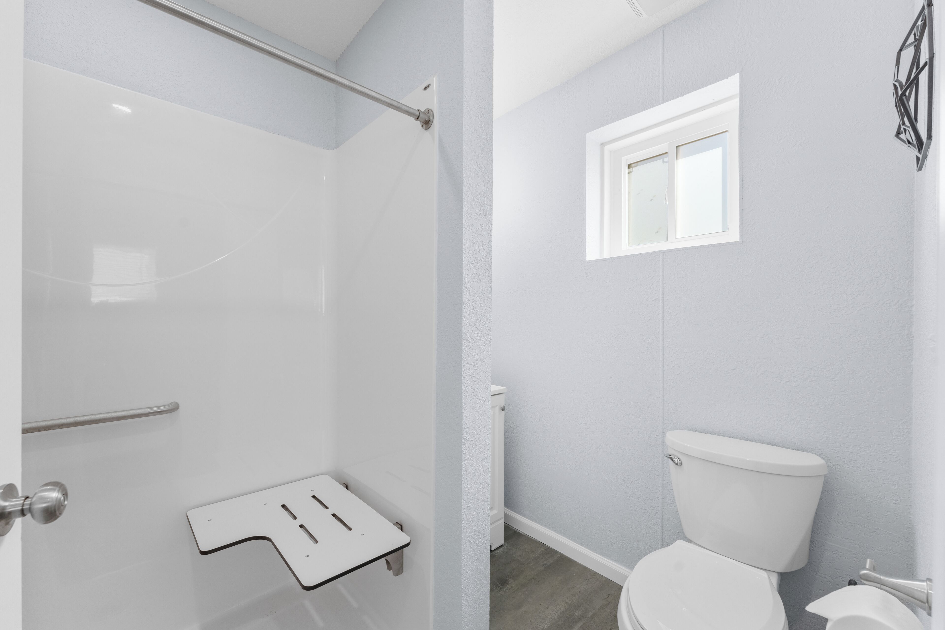 A bathroom with a shower, toilet, and a small window.