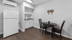 A modern kitchen with white cabinets, a built-in oven, and a dining area with a dark wooden table and chairs.