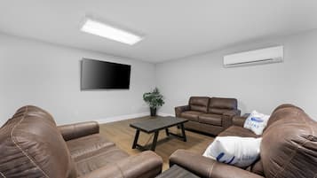 A living room with brown leather sofas, a wooden coffee table, a flat-screen TV, and an air conditioning unit.