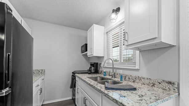 A modern kitchen with white cabinets, granite countertops, a stainless steel refrigerator, and a window with blinds. - Come stay at this modern 2 bedroom suite, located close to Table Rock Lake and Silver Dollar City. (Branson)