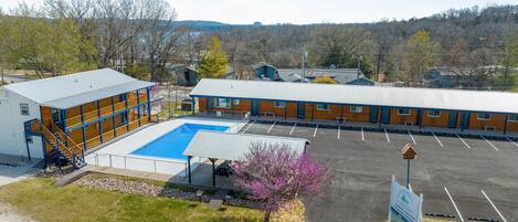 A hotel with a swimming pool, a parking lot, and a view of the surrounding landscape.