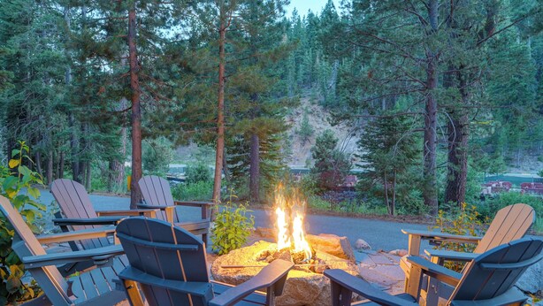 A fire pit surrounded by Adirondack chairs in a forested area.