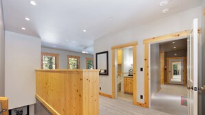 A spacious interior with a wooden staircase, multiple doors leading to different rooms, and a view of an outdoor area through a window.