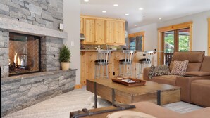 A modern living room with a stone fireplace, wooden kitchen cabinets, and a cozy seating area.