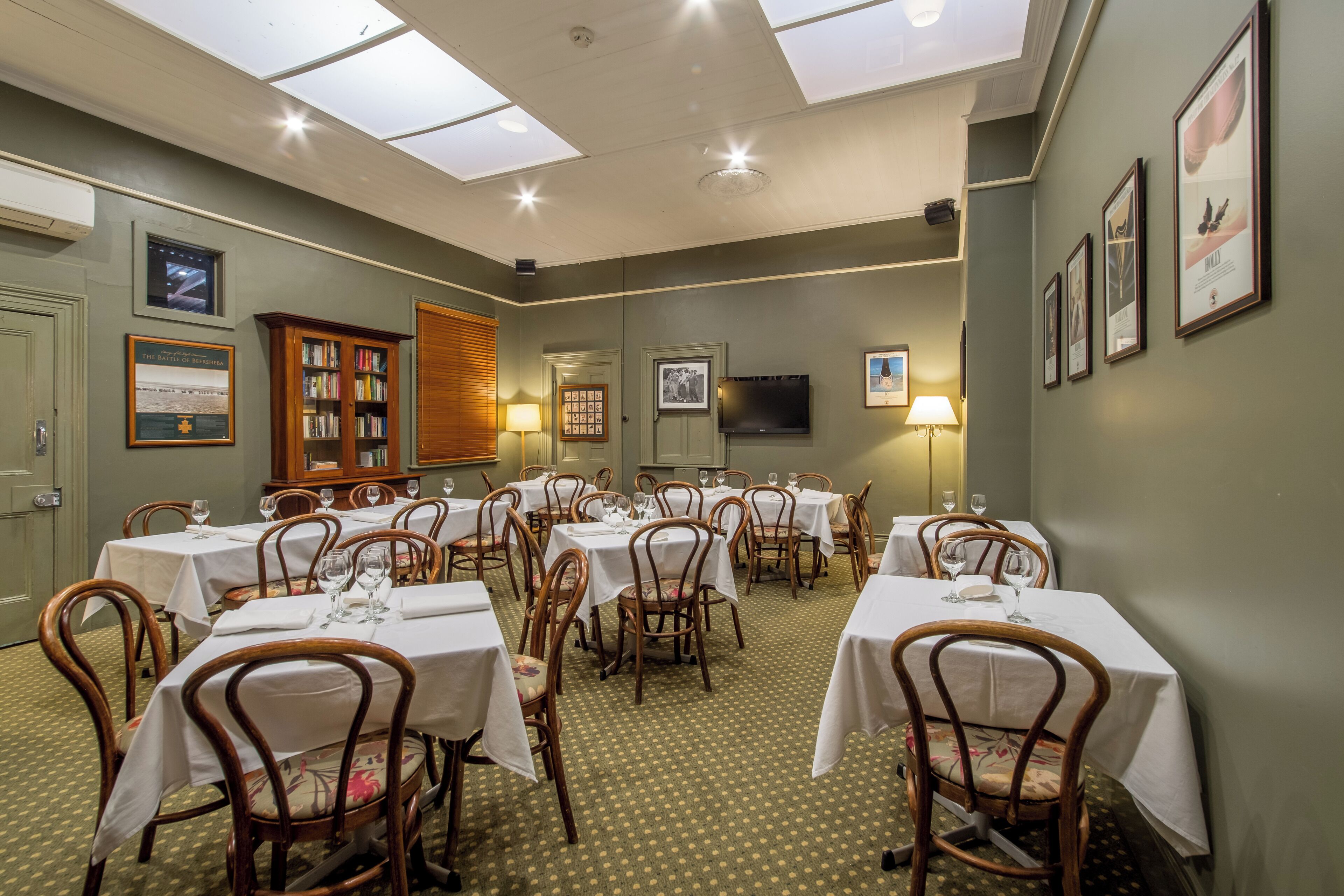 A dining area with multiple tables and chairs, a wooden cabinet, and framed pictures on the walls.