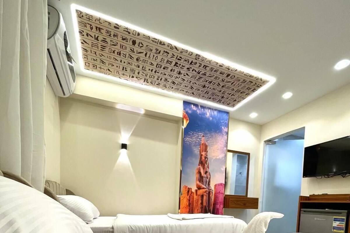 Ein Hotelzimmer mit einem großen Bett, einem Flachbildfernseher, einer Wand-Klimaanlage und einem Bild an der Wand.