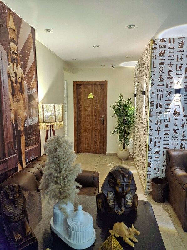 A modern lobby with a wooden door marked '201', a large Egyptian-themed painting, a potted plant, and a wall with hieroglyphics. - Miami Pyramids View (Giza)