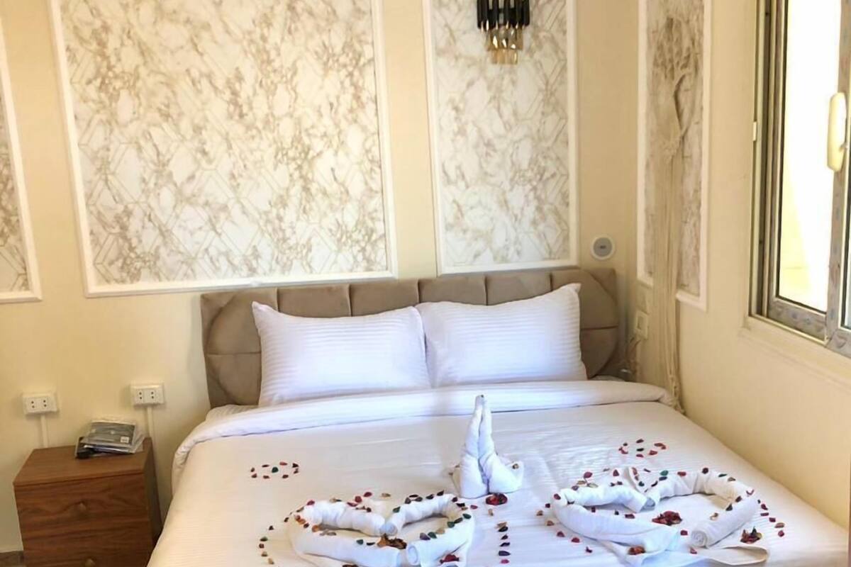 Ein ordentlich bezogenes Bett mit einem Kopfstück im Marmor-Design, ein Nachttisch mit einem Buch und eine Wandleuchte.