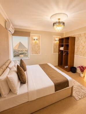 A bedroom with a bed, a wardrobe, a window with a view of a pyramid, and a chandelier.