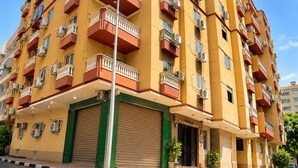 A multi-story residential building with balconies, air conditioning units, and a green entrance.