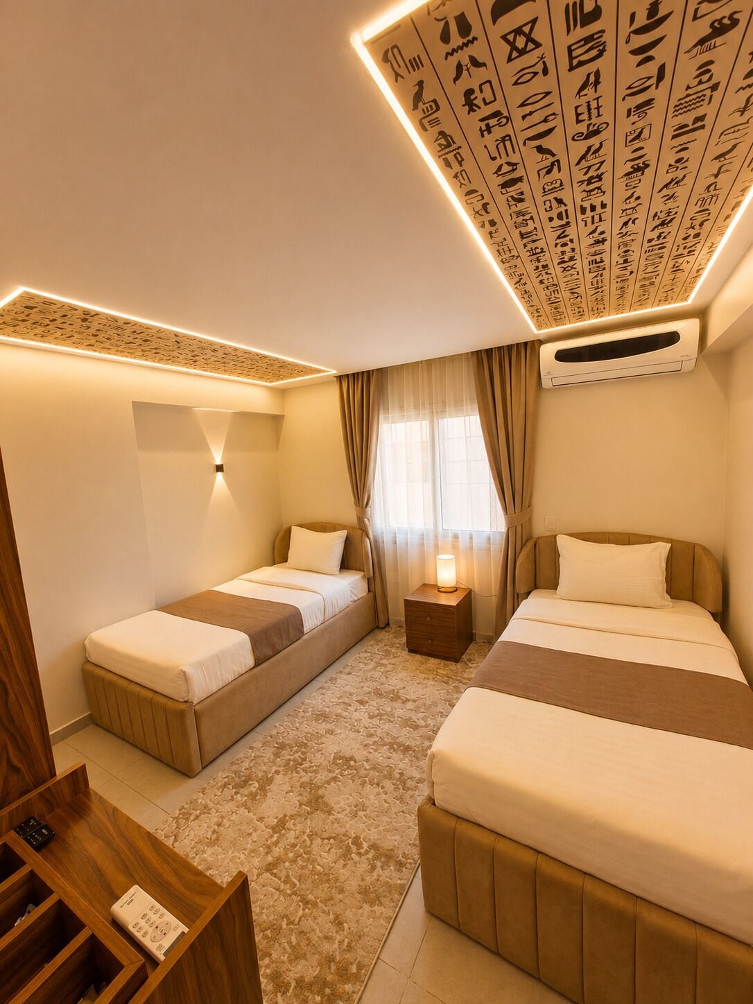 Een hotelkamer met twee bedden, een houten nachtkastje, een klein tafeltje en een airconditioner.