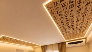 A hotel room with two beds, a wooden nightstand, a small table, and a wall-mounted air conditioning unit.