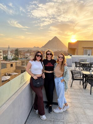 Three people on a rooftop terrace with a view of a pyramid and cityscape.