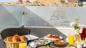 A breakfast table with various dishes, a glass of orange juice, and a view of the Pyramids of Giza.
