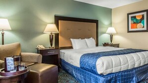 A hotel room with a large bed, two bedside tables with lamps, a chair, and a small table with a tray and glasses. - Regency Inn and Suites - Non Smoking King (New London)