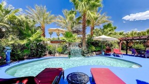 Un área de piscina con sillones de descanso, una cascada y palmeras.