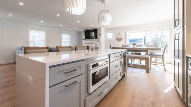 Een moderne keuken met een centraal eiland, inbouwapparatuur en hangende lampen.