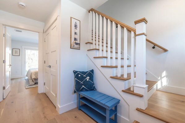 Un escalier avec des marches en bois et des rampes blanches, un banc bleu avec un coussin à motifs et un tableau encadré au mur.