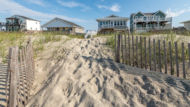 A beachfront property with multiple houses, a sandy beach, and a wooden fence.