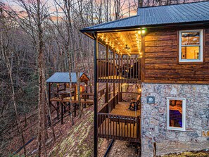 A cabin with a wooden exterior, stone foundation, and a balcony with string lights.