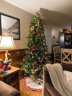 Un salon avec un sapin de Noël décoré, un tableau encadré accroché au mur et un coin salon confortable.