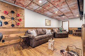 A cozy living room with a brown leather couch, wooden flooring, a dartboard, and a framed map on the wall.