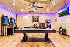 A pool table in a room with wooden walls, ceiling fan, and gaming machines. - Creek · Sauna & Hot Tub · Cabin · Game Room (Sevierville)