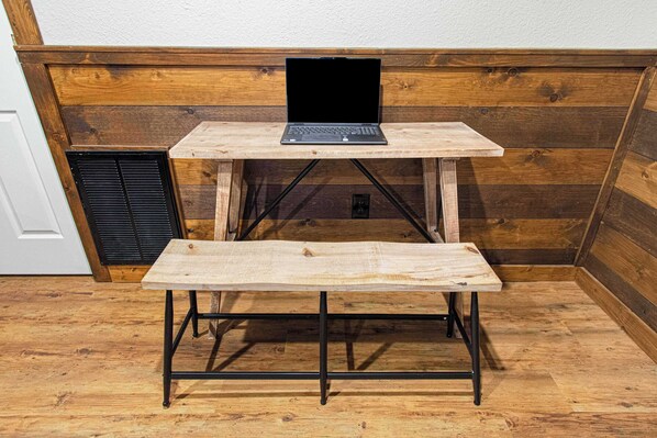 A wooden desk with a laptop, a bench, and a vent.