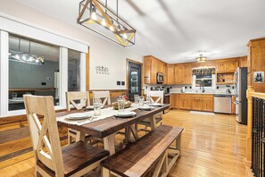 A modern kitchen with wooden cabinets, a dining area with a wooden table and chairs, and a large window.
