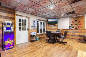 A room with a wooden floor, a dartboard, a television, and a gaming machine.