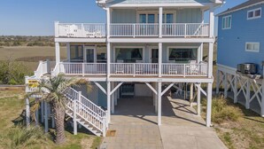 A two-story beachfront house with a balcony, a covered porch, and a view of the ocean.