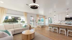 A modern living room with a sofa, a round wooden coffee table, and a dining area with a white table and bar stools.
