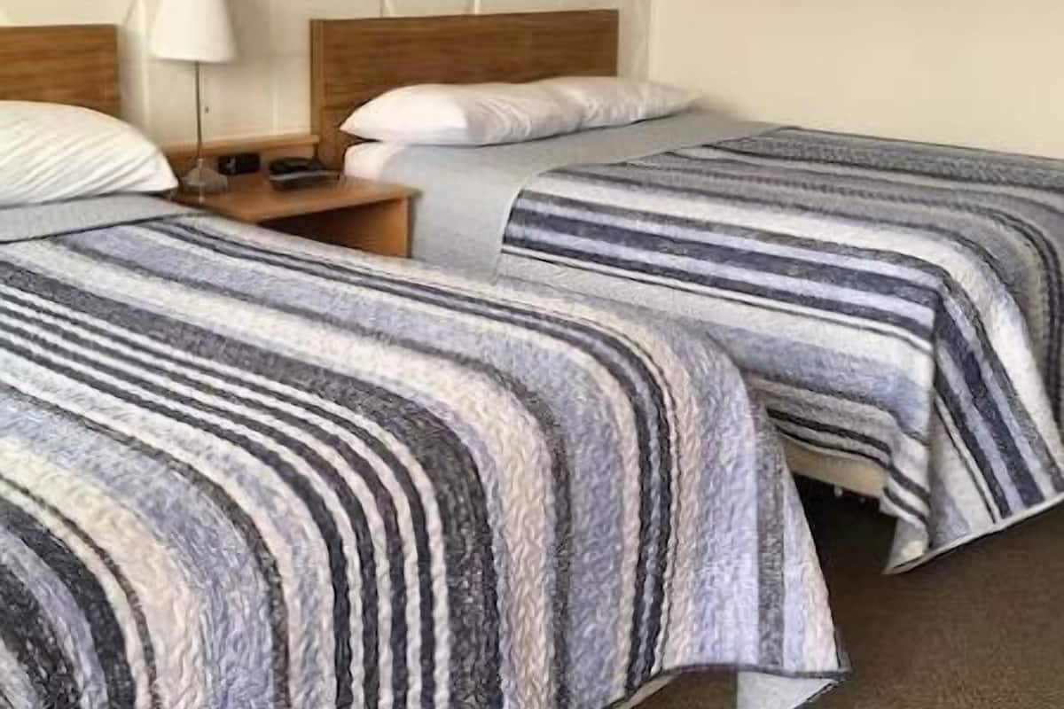 A hotel room with two beds, a nightstand, a lamp, and a painting on the wall.