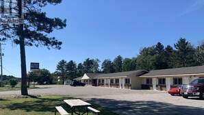 Un motel avec une table de pique-nique au premier plan, un parking et un camion rouge garé devant.