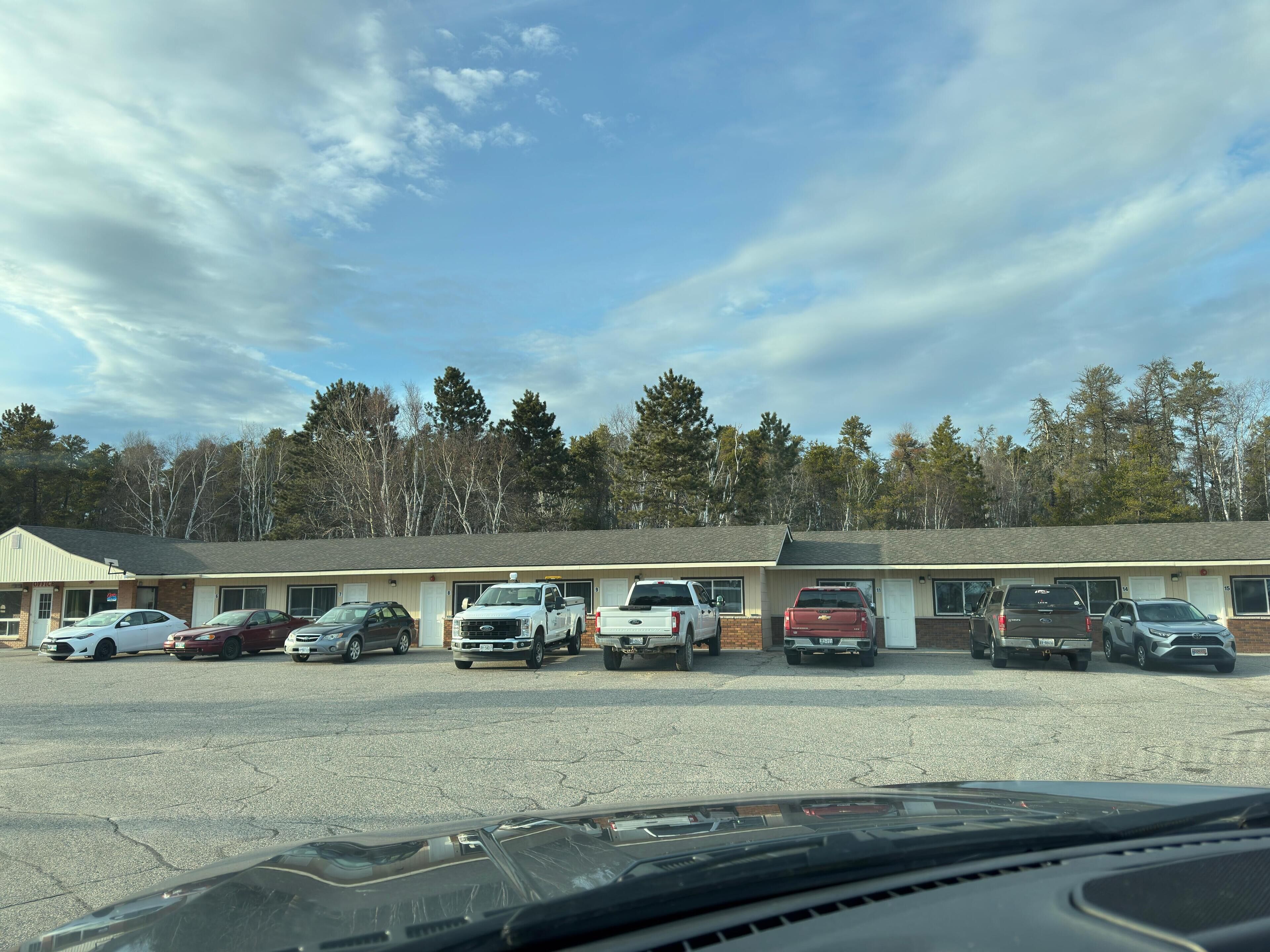 Un motel doté de nombreuses places de stationnement et où une rangée de véhicules est garée devant.