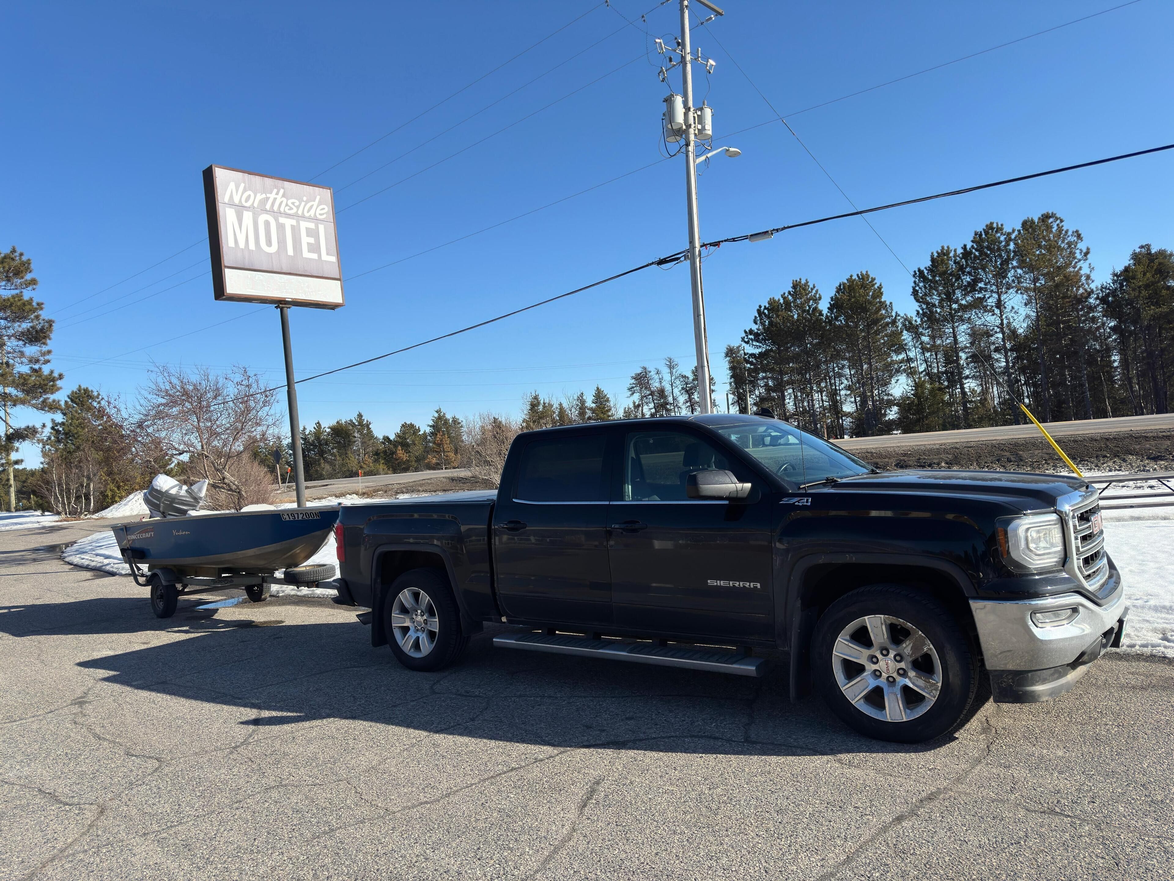 A black GMC Sierra pickup truck with a boat trailer attached, parked in front of a motel sign.