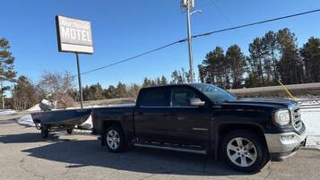 A black GMC Sierra pickup truck with a boat trailer attached, parked in front of a motel sign.