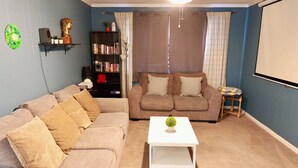 A living room with two sofas, a coffee table, a bookshelf, and a projector screen. - Cozy, gallery-inspired stay, 5min to Fort Liberty (Fayetteville)