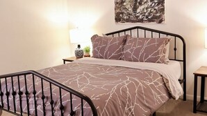 A bedroom with a bed, a ceiling fan, a wall-mounted painting, and bedside lamps. - Cozy, gallery-inspired stay, 5min to Fort Liberty (Fayetteville)
