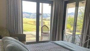 Ein Schlafzimmer mit einem großen Bett, einem Sessel und Blick ins Freie durch eine Schiebetür.