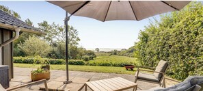 Un patio con mobili da esterno, un ombrellone grande e vista su un paesaggio verde.