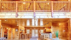 A spacious log cabin with a central open area, a balcony, and a kitchen area.