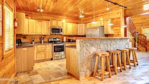 A wooden cabin-style kitchen with a stone island, bar stools, and a stone fireplace.