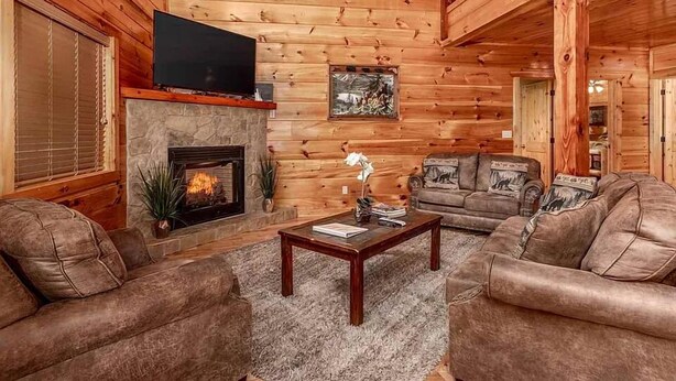 A cozy log cabin interior with a fireplace, a television, and a comfortable seating area.