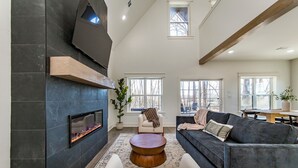 A modern living room with a fireplace, a sofa, a coffee table, and large windows.