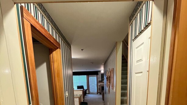 Un couloir doté d’un sol carrelé, de portes en bois et offrant une vue sur un salon avec un canapé et une fenêtre.