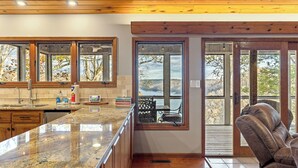 A kitchen with a granite countertop, wooden cabinets, and a view of the outdoors through large windows.