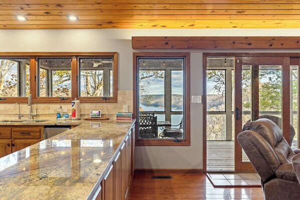 A kitchen with a granite countertop, wooden cabinets, and a view of the outdoors through large windows.