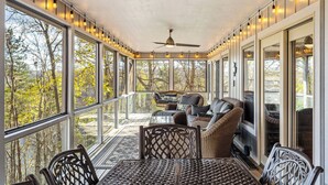 A sunroom with large windows, a ceiling fan, wicker furniture, and a view of trees.
