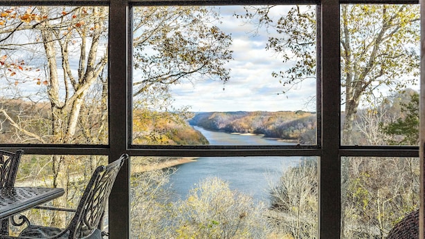A room with a large window offering a view of a river and surrounding trees.